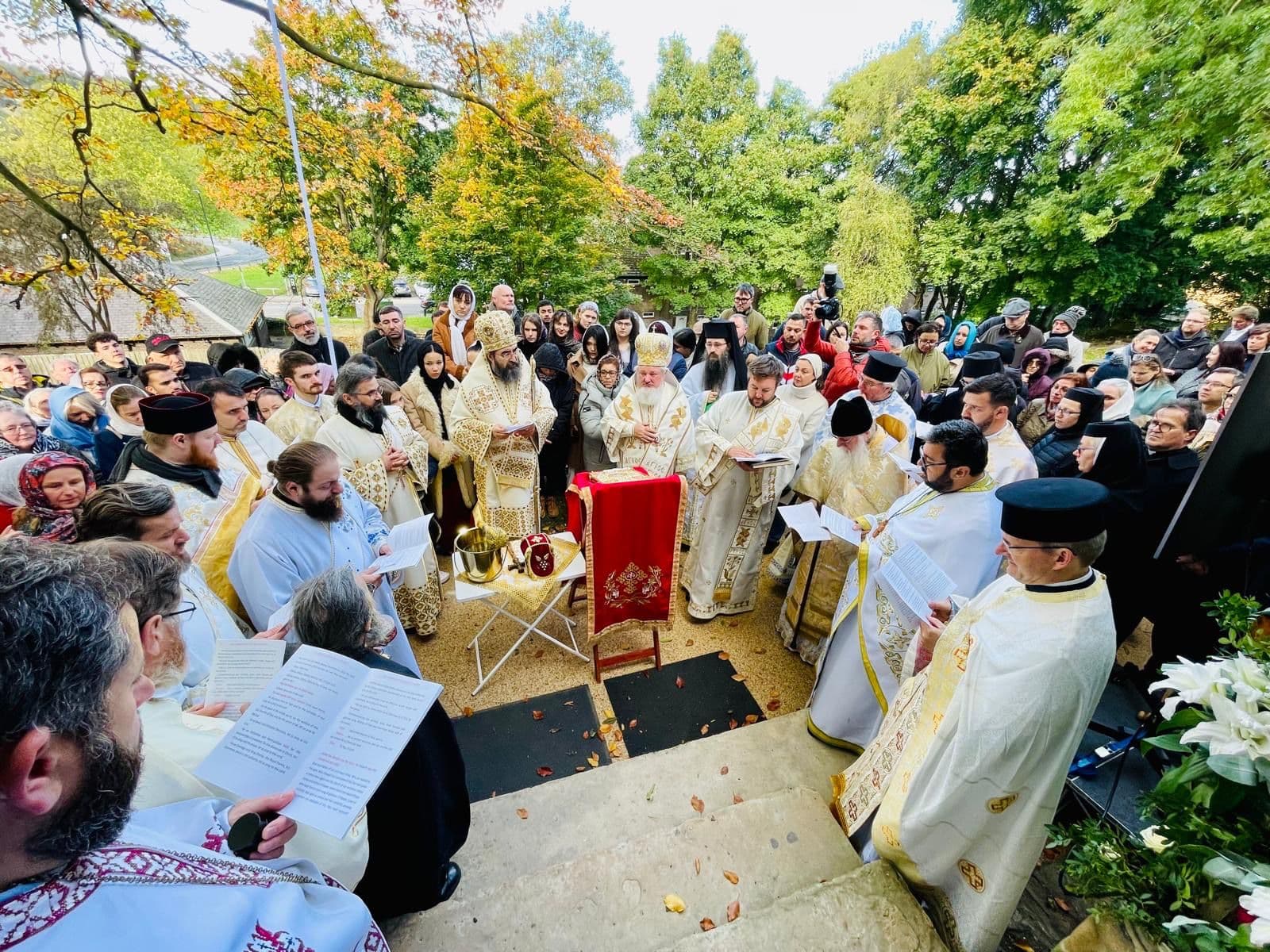 Clergy and faithful gathered around an outdoor altar beneath autumn trees