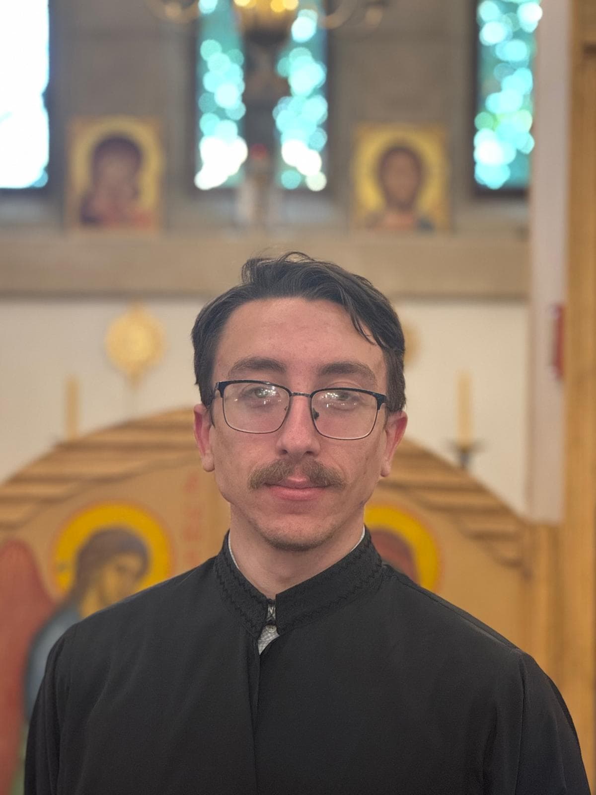 Reader Alex John Coleman, in a black cassock, before the iconostasis