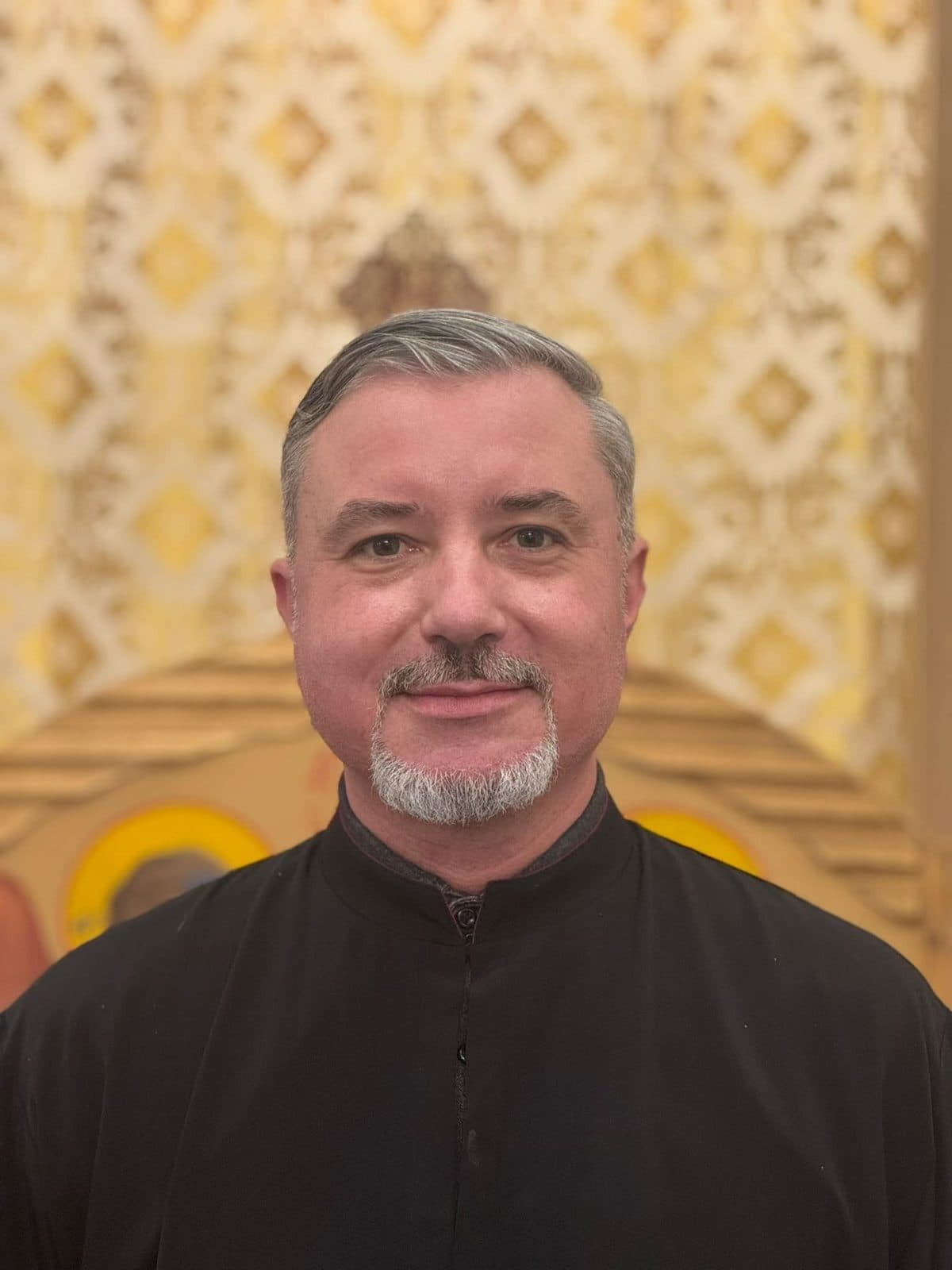 Reader Răzvan Alexandru, in a black cassock, before the iconostasis